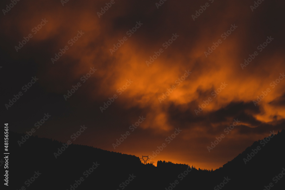 Epic dark orange sunset sky with threatening clouds in the Vosges mountains with a power line pylon in France