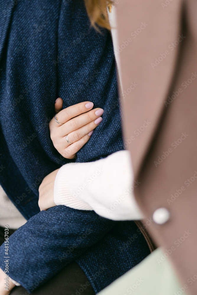 The woman in the coat is holding her man's hand, hugging him.