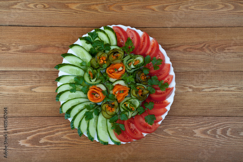 Beautifully sliced tomatoes and cucumbers, carrots on a round plate, for a festive table. Sliced vegetable salad. on a wooden background. close-up. food.