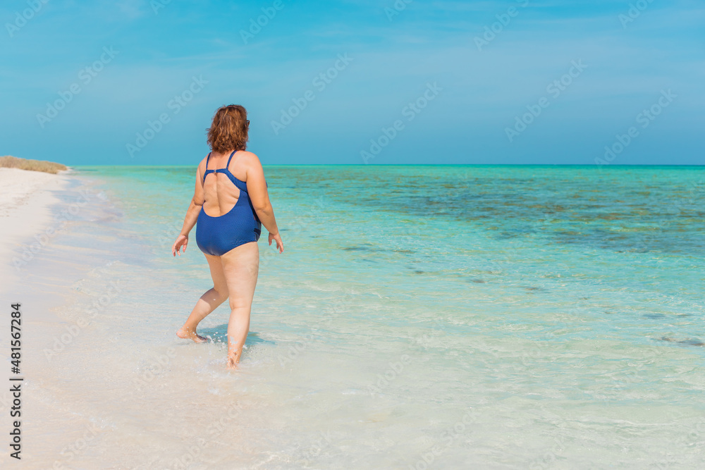 Body positive concept. Middle age lady at the beach in blue swimsuit resting and have a nice time