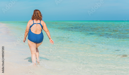 Body positive concept. Middle age lady at the beach in blue swimsuit resting and have a nice time