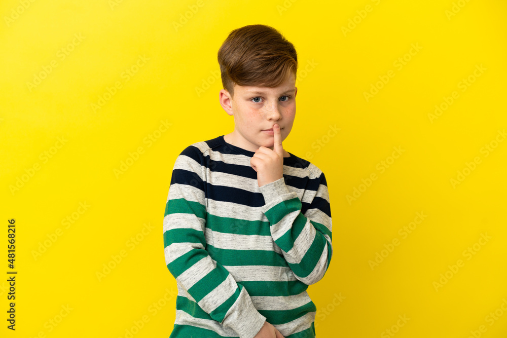 Little redhead boy isolated on yellow background having doubts while looking up Little redhead boy isolated on yellow background having doubts while looking up