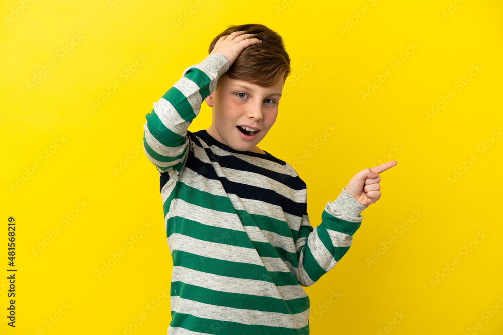Little redhead boy isolated on yellow background surprised and pointing finger to the side Little redhead boy isolated on yellow background surprised and pointing finger to the side