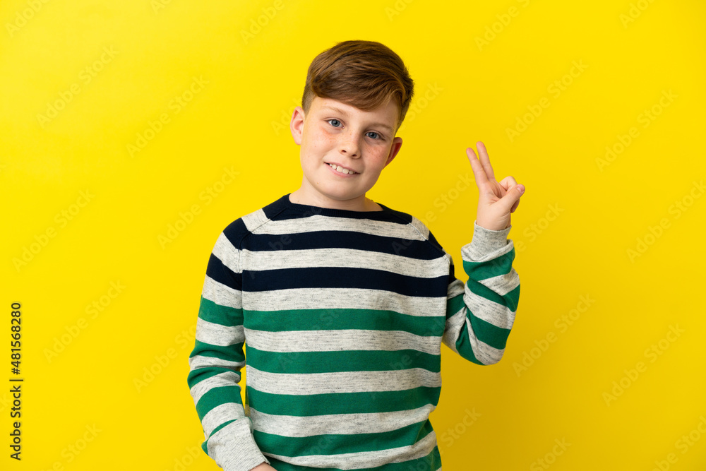 Little redhead boy isolated on yellow background smiling and showing victory sign Little redhead boy isolated on yellow background smiling and showing victory sign