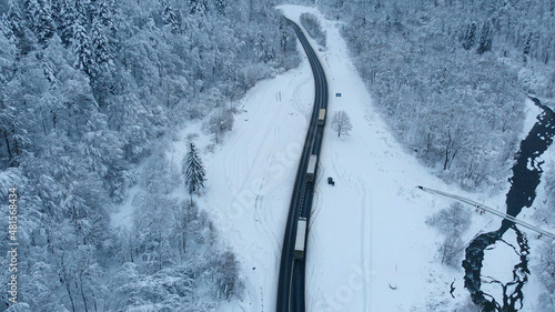 Aerial shot: Trucks driving by the road in winter forest. © Motionstocks