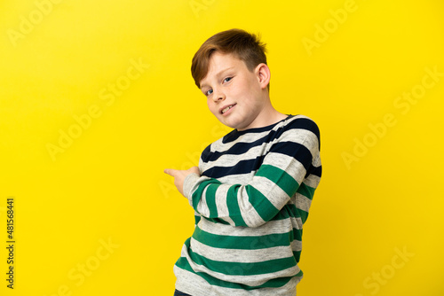 Little redhead boy isolated on yellow background pointing back