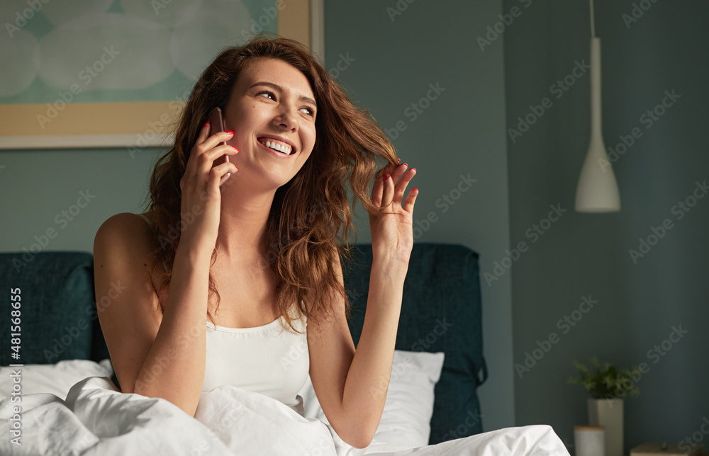 Happy woman having phone conversation sitting on bed in morning Happy woman having phone conversation sitting on bed in morning