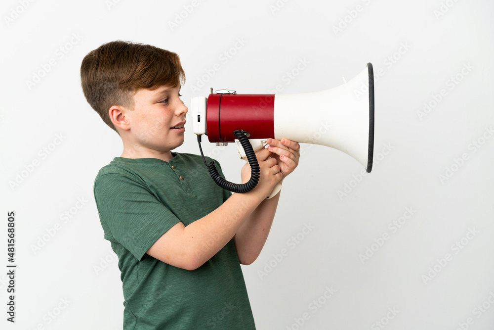 Naklejka premium Little redhead boy isolated on white background shouting through a megaphone to announce something