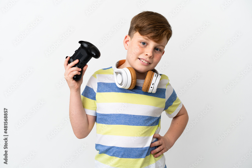 Little redhead boy holding a game pad isolated on white background posing with arms at hip and smiling Little redhead boy holding a game pad isolated on white background posing with arms at hip and smiling