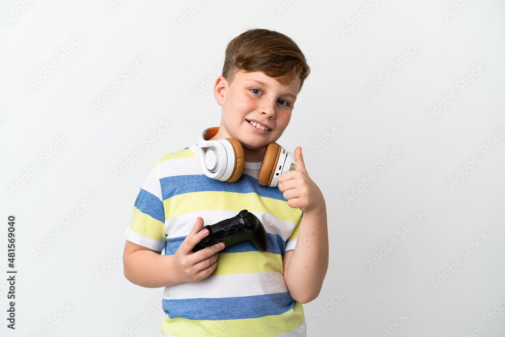 Little redhead boy holding a game pad isolated on white background giving a thumbs up gesture Little redhead boy holding a game pad isolated on white background giving a thumbs up gesture