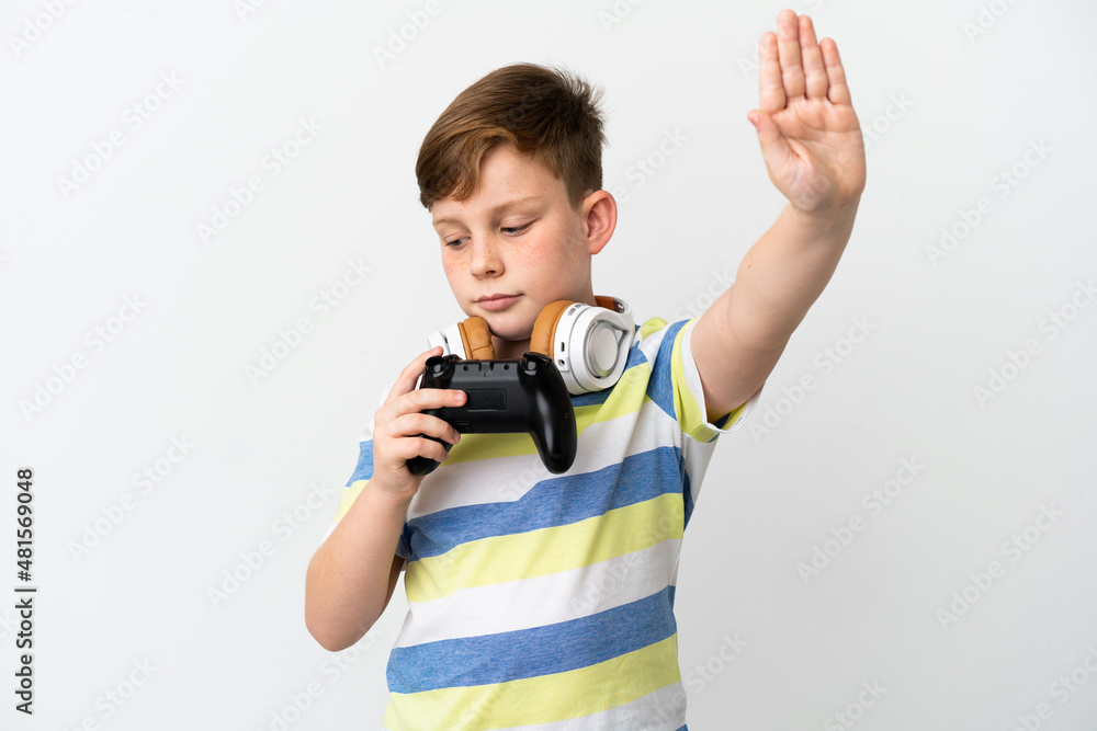 Little redhead boy holding a game pad isolated on white background making stop gesture and disappointed Little redhead boy holding a game pad isolated on white background making stop gesture and disappointed