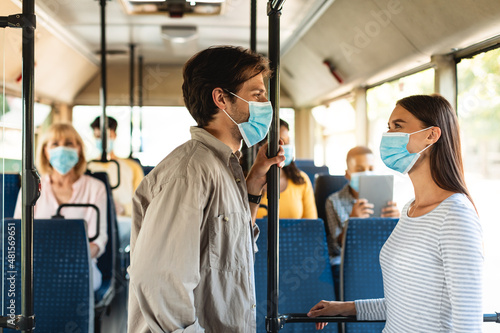 Beautiful smiling couple in masks standing in bus and talking