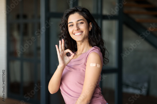 Young woman with band aid on arm after coronavirus vaccination showing okay, recommending covid-19 vaccine shot at home