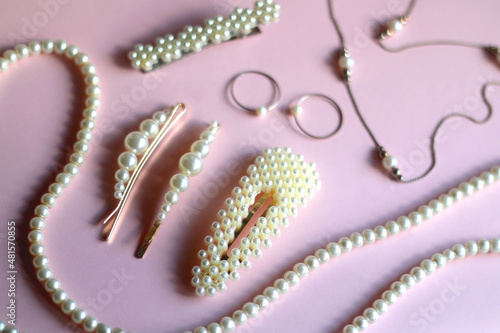 Various pearl jewelry and hair accessories on pink background. Selective focus.
