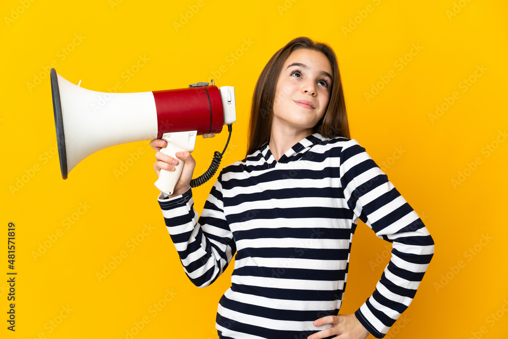 Naklejka premium Little girl isolated on yellow background holding a megaphone and thinking