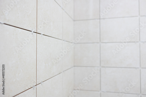 Installation and alignment of ceramic tiles in a white bathroom. Placed the plastic crosses between the tiles.