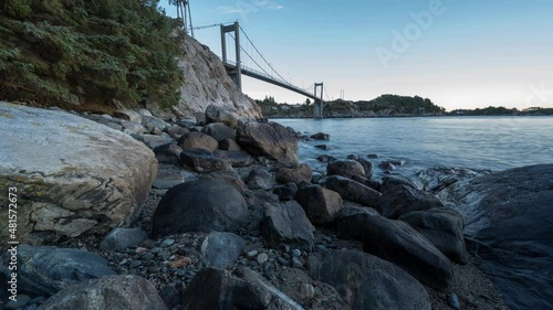 Day to night time lapse transition view of Herdla bridge, Askoy, Norway low angle view of water, rocks and sky. Scenic beauty of Norway waterside as daytime turns to night and lights come on pan left photo