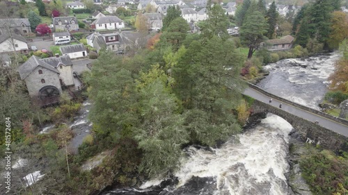Aerial drone footage descending over fast flowing water and river rapids at the Falls of Dochart in Killin, Trossachs National Park, Scotland with white water, rocks and surrounded by native trees photo
