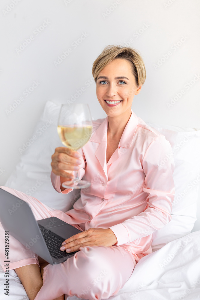 Happy woman sitting on bed using pc drinking wine Happy woman sitting on bed using pc drinking wine