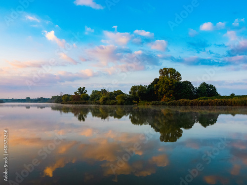 Morning sky with clouds over the river. Beautiful sunrise and reflecting clouds in a river. Nature landscape, reflection, blue and pink color sky, landscape during dawn