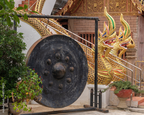 Big black gong hanging in metal frame with golden naga in background at historic ancient Wat Chiang Yuen buddhist temple, Chiang Mai, Thailand