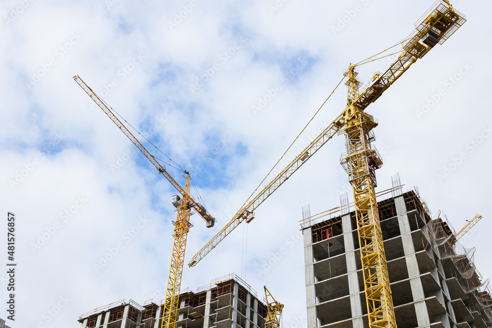 Construction of high monolithic frame buildings made of reinforced concrete. The work of high-rise construction cranes on the background of the house under construction.