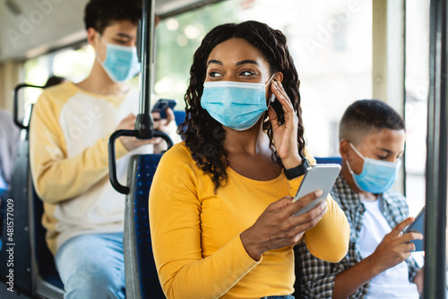 Smiling black woman in facemask listening music in bus