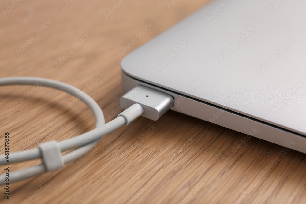 Modern laptop and charging cable on wooden table, closeup Modern laptop and charging cable on wooden table, closeup