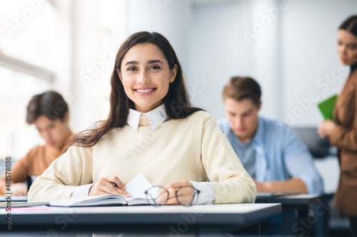 Fotografia Smiling student sitting at desk in classroom posing at camera