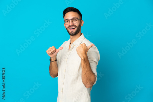 Young caucasian man isolated on blue background pointing to the side to present a product