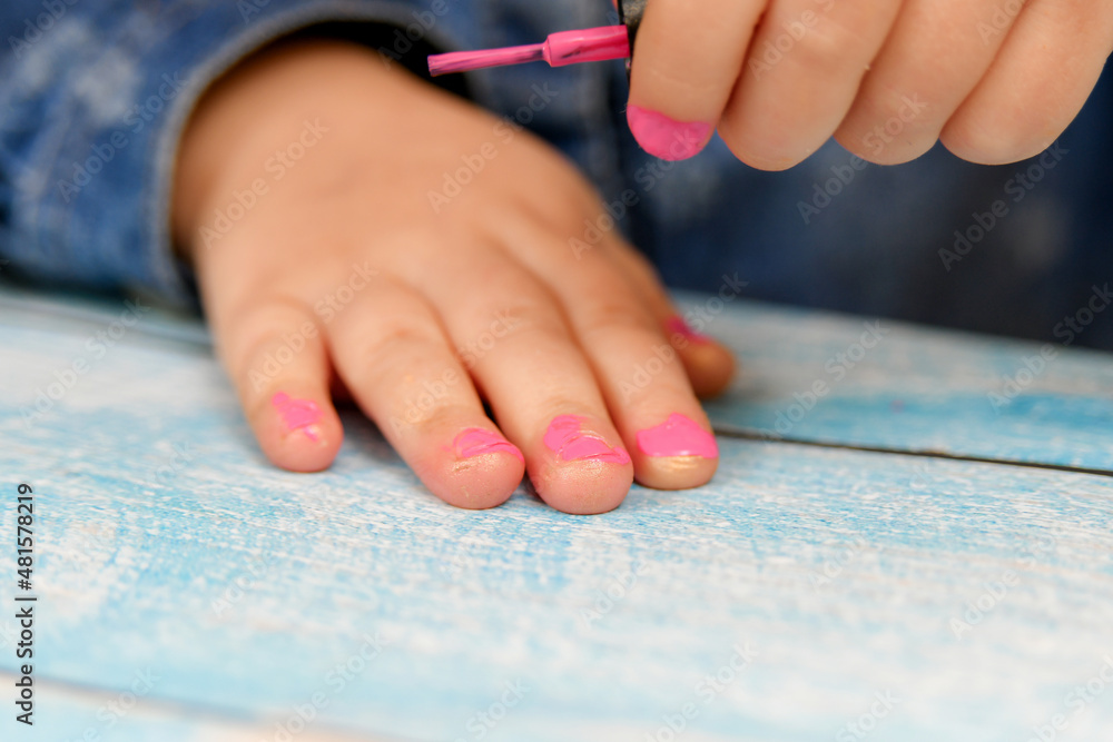 Fototapeta premium A small child looks with attention at his painted nails with nail polish.