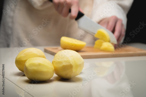 Close-up of female hands cutting fresh peeled potatoes on a cutting wooden board. Vegetarian food preparation