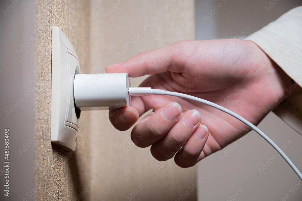 Close-up of a woman's hand inserting a white usb charger into a 220 volt socket
