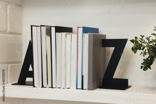 Decorative bookends with books and houseplant on shelf indoors photo