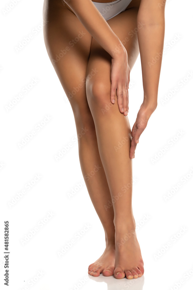 Woman applying a skin produst on her legs on a white Woman applying a skin produst on her legs on a white