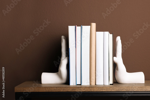 Konstfotografi Beautiful hand shaped bookends with books on shelf near brown wall