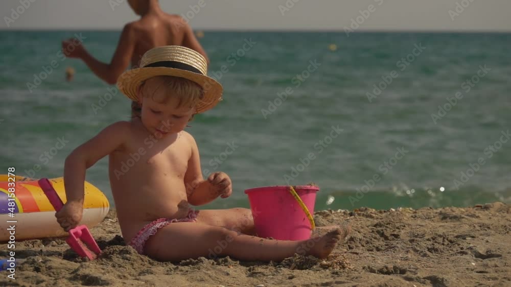 Cute little girl in a straw hat builds a sandcastle on the beach Cute little girl in a straw hat builds a sandcastle on the beach