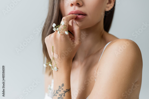 cropped view of young woman with tiny flowers on tattooed hand isolated on grey.