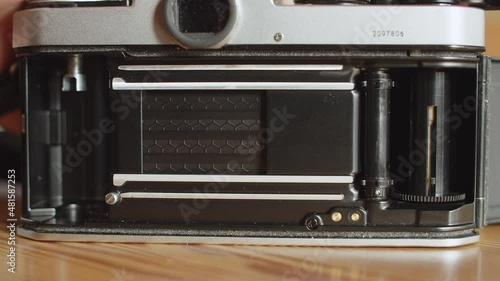 View on the opened back of an analog camera. The shutter with an honeycomb-pattern gets reset/cocked, the film take up spool rotates as the film advance lever gets wound and the shutter gets fired photo