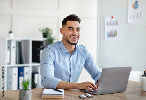 Attractive young Arab businessman using laptop pc at his desk in home office