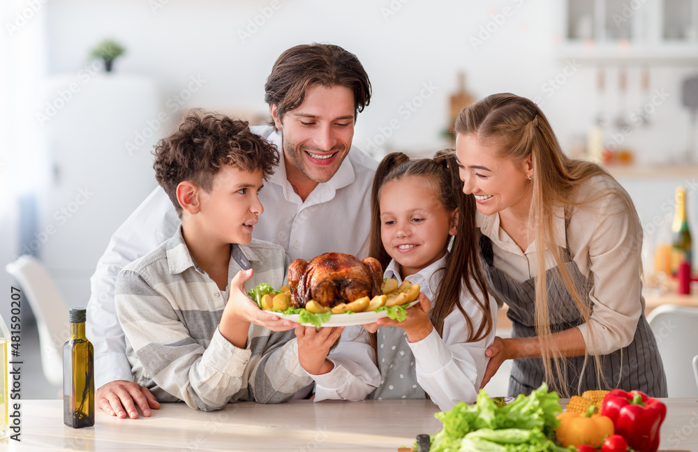 Cheerful children with parents cooking traditional dinner together, holding roast turkey for holiday meal at kitchen Cheerful children with parents cooking traditional dinner together, holding roast turkey for holiday meal at kitchen