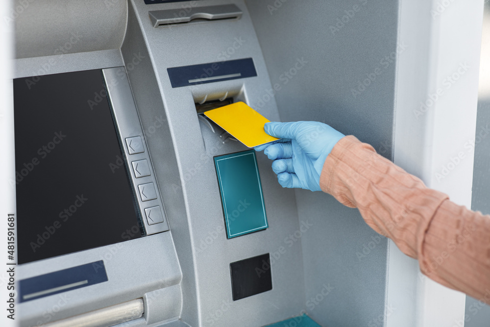 Cropped young islamic female in rubber glove inserts credit card into ATM to withdraw money outdoor, close up Cropped young islamic female in rubber glove inserts credit card into ATM to withdraw money outdoor, close up