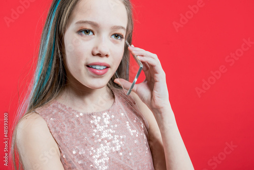 Beautiful girl talking on the phone on a red background. Schoolgirl gossip on cell phone. The teenager communicates on a cell phone with his friends