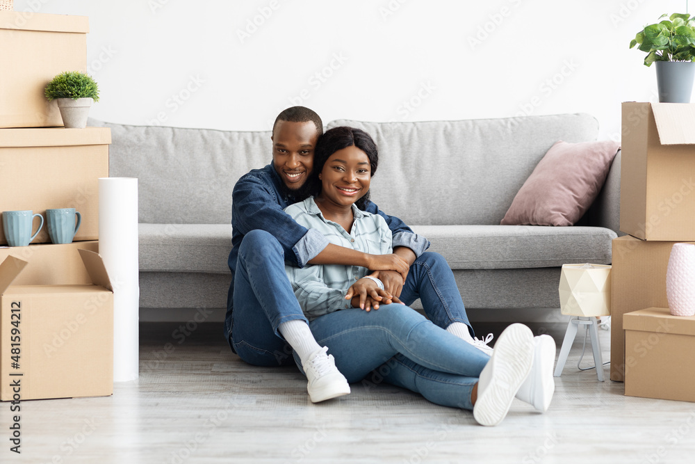 Happy african-american couple sitting in room with cardboard boxes on moving day Happy african-american couple sitting in room with cardboard boxes on moving day