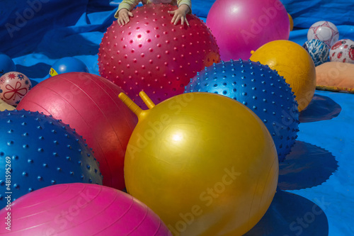 The hands of a small child are lying on a huge inflatable ball. Huge multicolored fitness balls. Photo outdoors.
