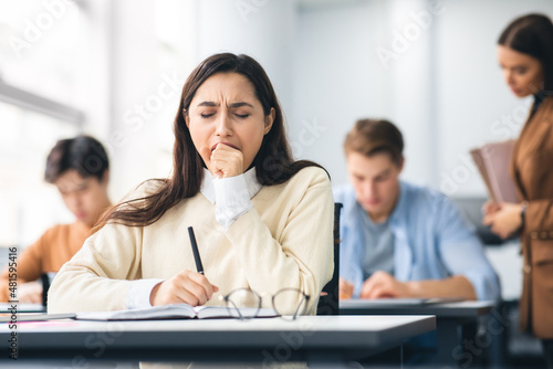Female student yawning sitting at desk in class photo