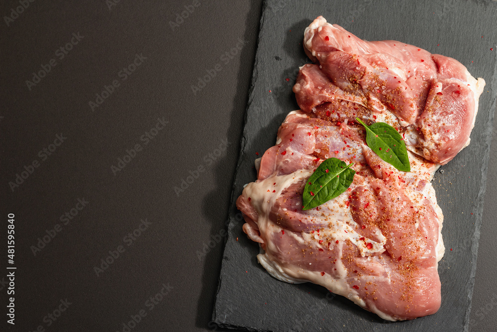Raw turkey thigh with spices. Fresh boneless meat on a ceramic stand. Hard light, dark shadow Raw turkey thigh with spices. Fresh boneless meat on a ceramic stand. Hard light, dark shadow