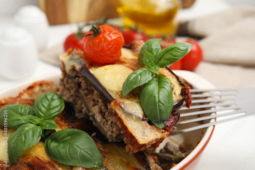 Spatula with piece of delicious eggplant lasagna over baking dish at table, closeup Spatula with piece of delicious eggplant lasagna over baking dish at table, closeup