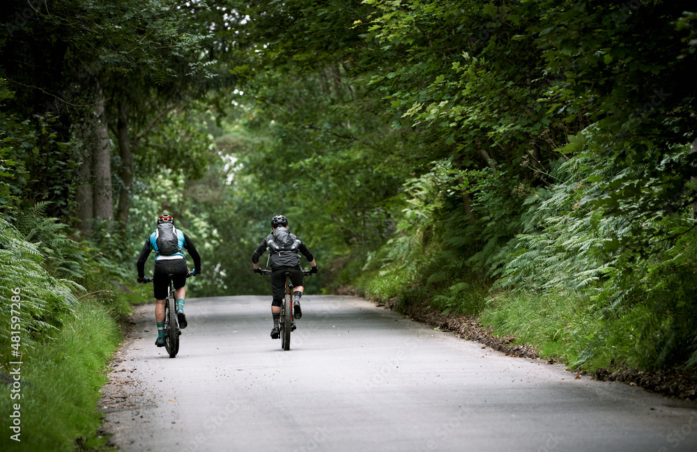The backs of two mountain bike cyclists riding up a steep road hill, Bale Hill, near Blanchland in County Duram. The backs of two mountain bike cyclists riding up a steep road hill, Bale Hill, near Blanchland in County Duram.