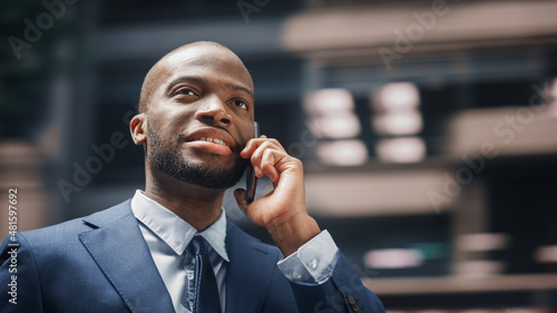 Street Shot: Portrait of Happy Black Businessman Talking on Smartphone in City. Successful African American Entrepreneur Using Mobile to Make a Phone Call. Blur Motion Background.